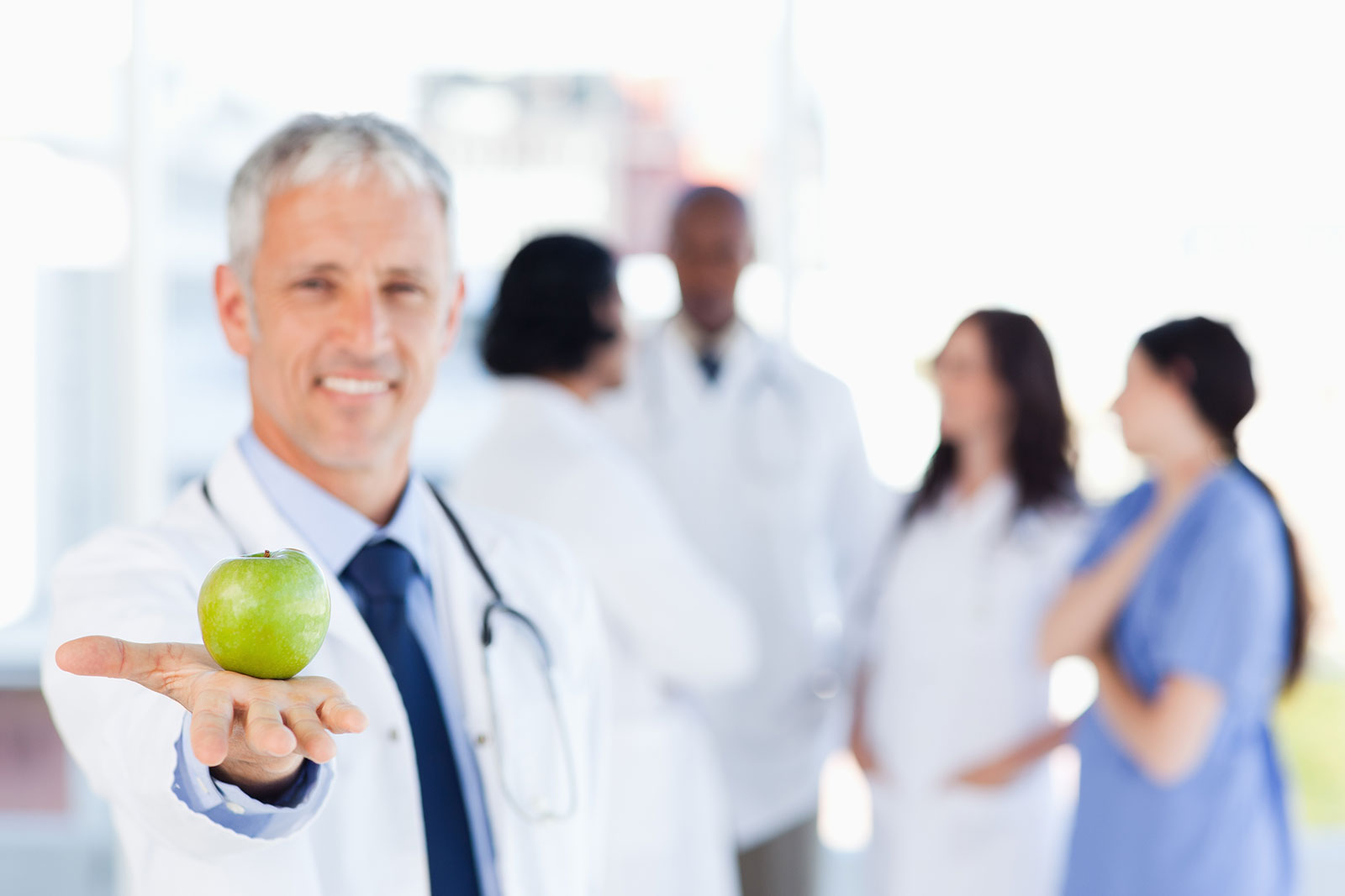 A doctor shows an apple to illustrate staying healthy and the relation between patient and the doctor.